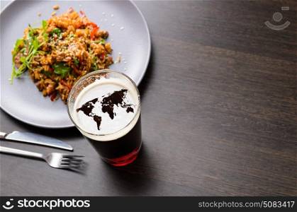 World map silhouette on foam in beer glass on black table with food, view from above. Elements of this image furnished by NASA