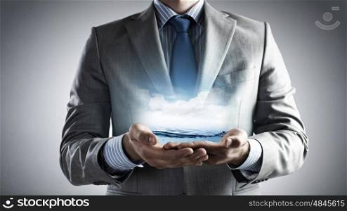World ocean. Close up of businessman holding clear blue water in palms