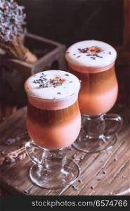 World of coffee pleasure. Photo close-up of two large glasses of fragrant latte with lavender grains on a wooden stand