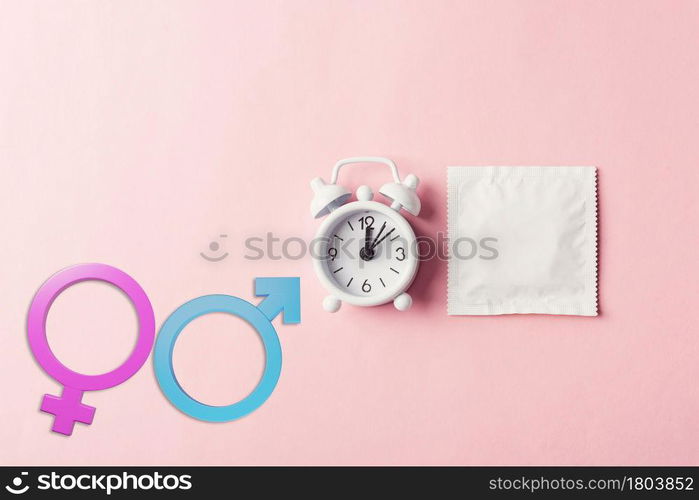 World sexual health or Aids day, condom in wrapper pack and Alarm clock birth control and Male and female gender signs, studio shot isolated on a pink background, activism and relationship sex concept