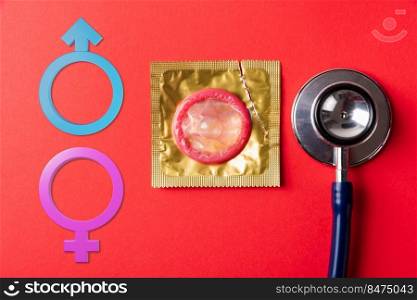 World sexual health or Aids day. Top view flat lay Male, female gender signs, medical equipment, condom in pack and stethoscope on a red  background, Safe sex and reproductive health concept