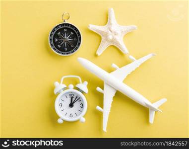 World Tourism Day, Top view flat lay of minimal toy model plane, airplane, starfish, alarm clock and compass, studio shot isolated on a yellow background, accessory flight holiday concept