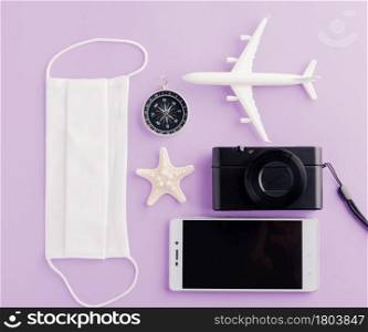 World Tourism Day, Top view of minimal model plane, airplane, starfish, compass, smartphone blank screen and face mask isolated on purple background, accessory flight holiday under coronavirus concept