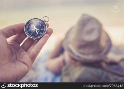 World travelling: Compass in the foreground, girl lying on the beach in the blurry background