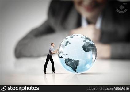 Worldwide business. Businesswoman looking at miniature of woman rolling Earth planet