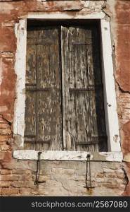 Worn building with window with closed wooden shutters in Venice, Italy.
