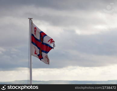 Worn flag of the Royal National Lifeboat Institution blows in the wind on a cloudy day