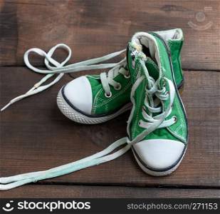 worn old textile green sneakers with untied white laces on a brown wooden background