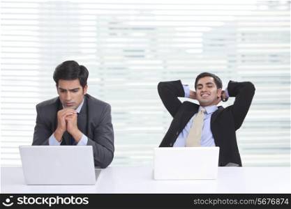 Worried businessman using laptop with colleague relaxing at desk in office