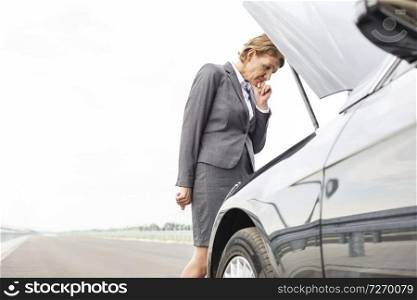 Worried businesswoman looking at breakdown car on road against sky