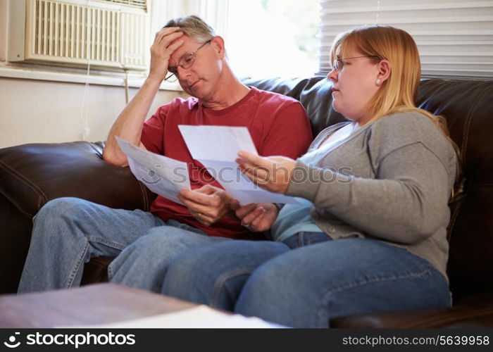 Worried Couple Sitting On Sofa Looking At Bills