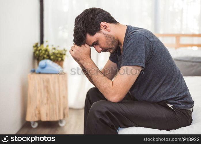 Worried man sitting on bed with hand on forehead in bedroom in serious mood emotion. Major Depressive Disorder called MDD concept. Lonely symptom of men alertness. Physical healthcare and social issue