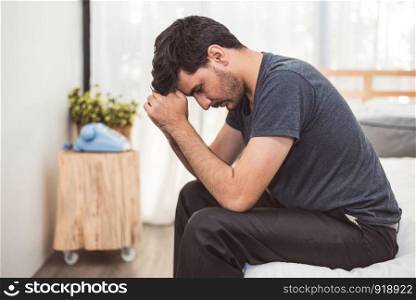 Worried man sitting on bed with hand on forehead in bedroom in serious mood emotion. Major Depressive Disorder called MDD concept. Lonely symptom of men alertness. Physical healthcare and social issue