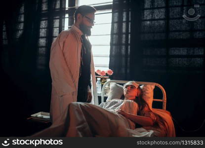 Worried man standing against ill loved woman in hospital bed. Illness of female patient in clinic room, health recovery and treatment. Man standing against ill woman in hospital bed