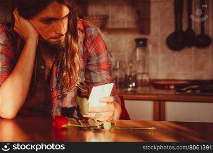 Worried man with rose and mobile phone.. Disappointment and depression. Unrequited love concept. Young worried disappointed man with single red rose and smartphone mobile phone waiting for his girlfriend.