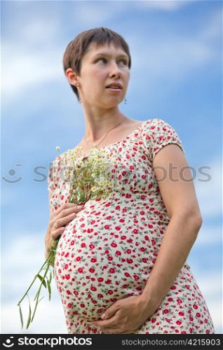 Worried pregnant woman with chamomile bouquet on sky background