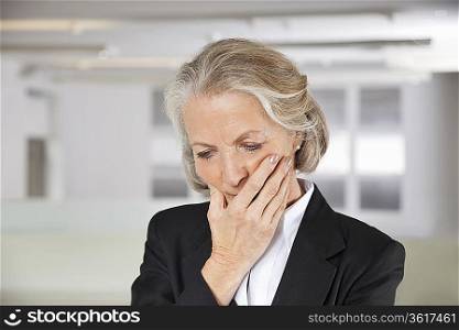 Worried senior businesswoman with hand on mouth in office