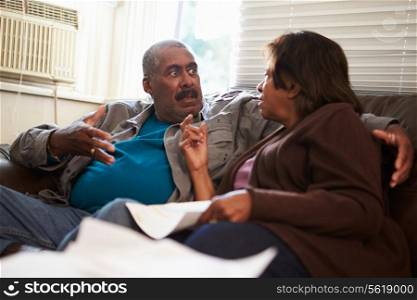 Worried Senior Couple Sitting On Sofa Looking At Bills