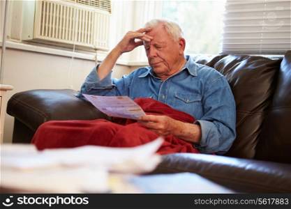 Worried Senior Man Sitting On Sofa Looking At Bills