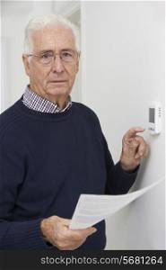 Worried Senior Man With Bill Turning Down Central Heating Thermostat