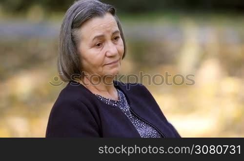 Worried senior woman in depression outdoors in park.