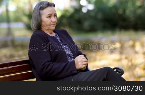 Worried senior woman in depression rubbing her hands outdoors in park.