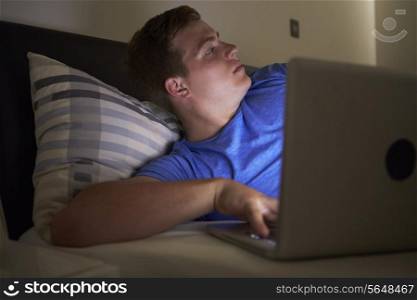 Worried Teenage Boy Using Laptop In Bed At Night