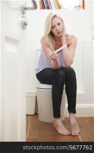 Worried Teenage Girl Sitting In Bathroom With Pregnancy Test