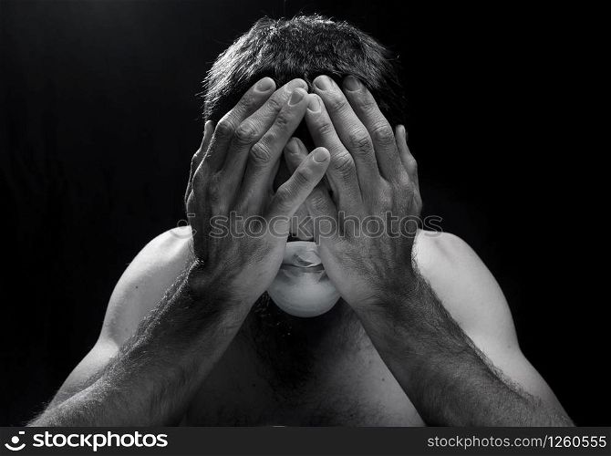worried white man with hands in head and surgical mask in trouble in a dark room or black background.concept of sadness