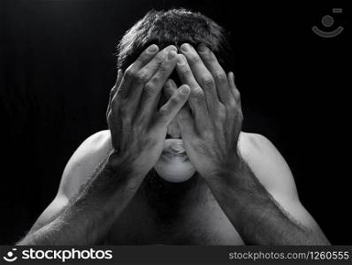 worried white man with hands in head and surgical mask in trouble in a dark room or black background.concept of sadness