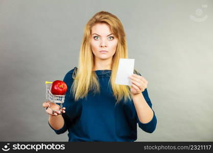 Worried woman holding shopping basket with fruits looking at bill receipt being scared of huge prices. Worried woman holding shopping basket with fruits