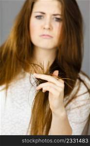 Worried woman looking at her dry split long brown hair ends, thinking of good treatment. Haircare and hairstyling concept.. Worried woman looking at her dry hair ends