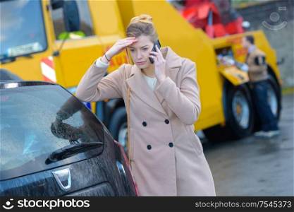 Worried woman on telephone, breakdown lorry in background