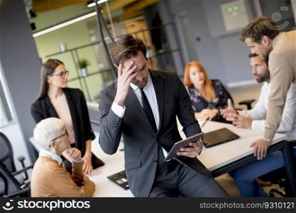 Worried young businessman using digital tablet in office in front of his team