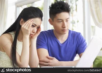 Worried Young Chinese Couple Sitting At Desk And Using Laptop At Home