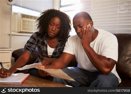 Worried Young Couple Sitting On Sofa Looking At Bills