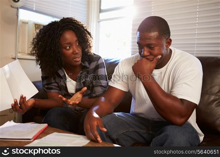 Worried Young Couple Sitting On Sofa Looking At Bills