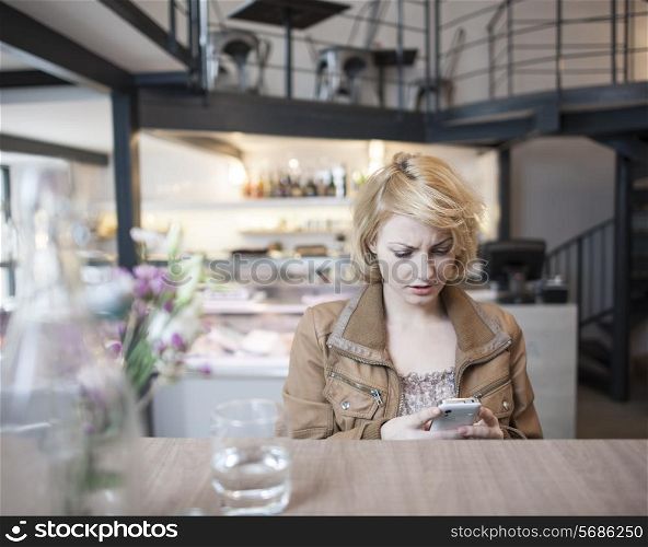 Worried young woman reading text message on cell phone in cafe