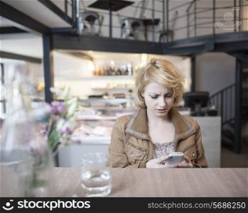 Worried young woman reading text message on cell phone in cafe