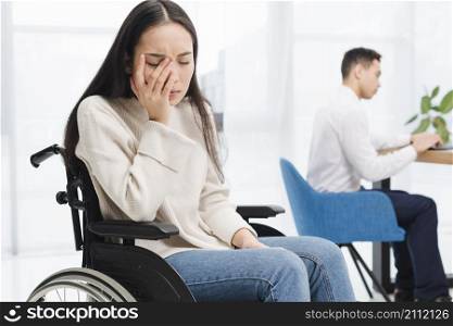 worried young woman sitting wheel chair sitting front male colleague using laptop
