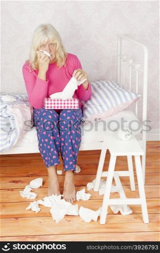 Worrying female with pink pajama and tissues sitting on bed