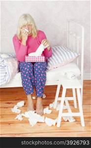 Worrying female with pink pajama and tissues sitting on bed