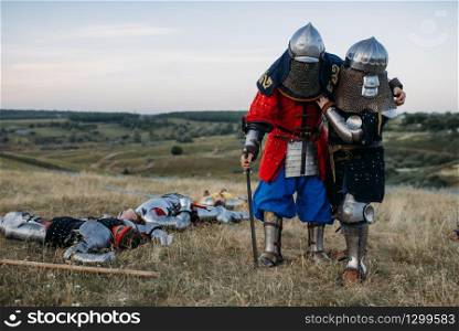 Wounded medieval knights in armor looks at the dead after great battle. Armored ancient warrior in armour posing in the field
