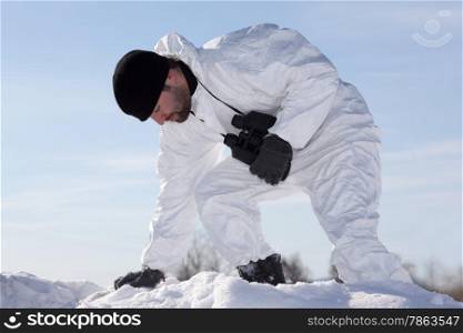 Wounded soldier in white camouflage sneaking through the mountains. Against the background of blue sky in winter sunny day