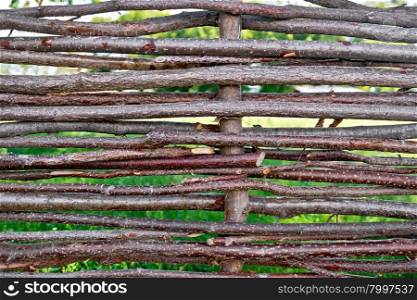 Woven willow fence with green grass in the gaps between the bars