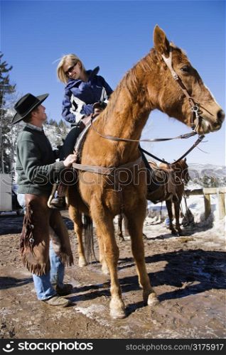 Wrangler talking to young Caucasian woman on horsebaclk.