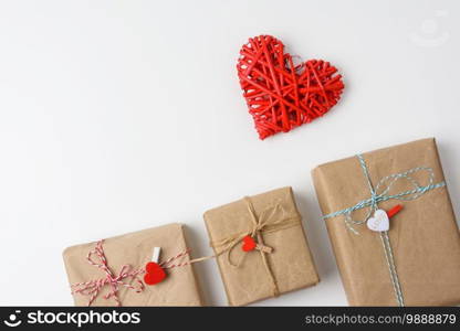 wrapped gifts in brown paper and a red wicker heart on a white background, top view. Valentine’s Day surprise