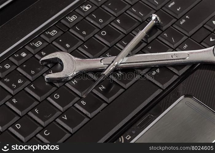 wrench tool and screwdrivers over a laptop, repair service concept