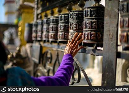 Wrinkled hand of an old woman touching Buddhist Prayer wheels at Swyamabhunath Stupa in Nepal