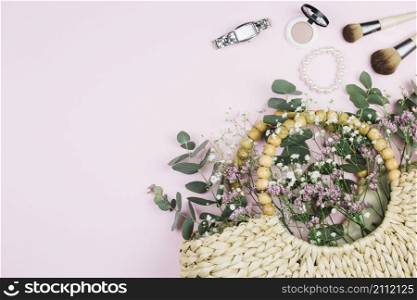 wrist watch makeup brush pearls bracelet compact face powder with limonium gypsophila flowers wicker bag against pink background